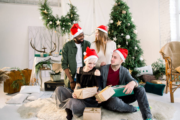 Group of happy multiracial friends laughing and sharing Christmas gifts in beautiful cozy studio - Photo, image