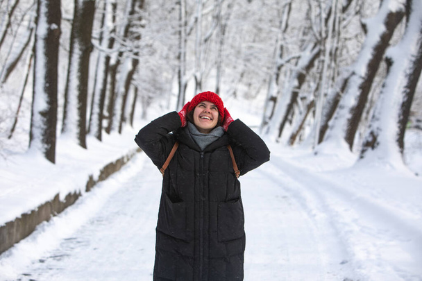 młoda ładna uśmiechnięta kobieta w płaszczu zimowym z czerwonym kapeluszem w parku leśnym miasta - Zdjęcie, obraz