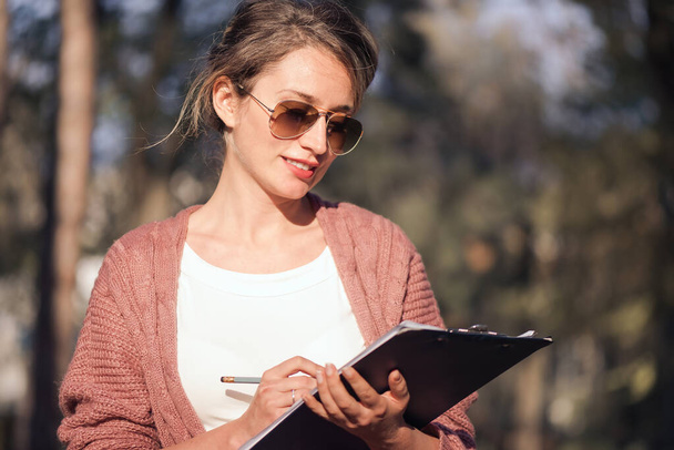 Szczęśliwa uśmiechnięta kobieta w okularach przeciwsłonecznych pracująca z papierami - Zdjęcie, obraz