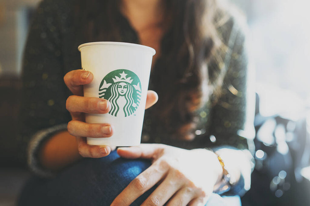 New York, USA - November 5, 2019 : Close up of a Woman drinking a tall Starbucks coffee in starbucks coffee shop with carrot cake. Starbucks is the world's largest coffee house with over 20,000 stores - 写真・画像