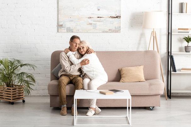 старший чоловік обіймає хвору дружину з психічними захворюваннями, сидячи на дивані вдома
  - Фото, зображення