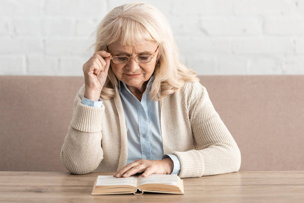 senior woman with alzheimer disease reading book and touching glasses - Φωτογραφία, εικόνα