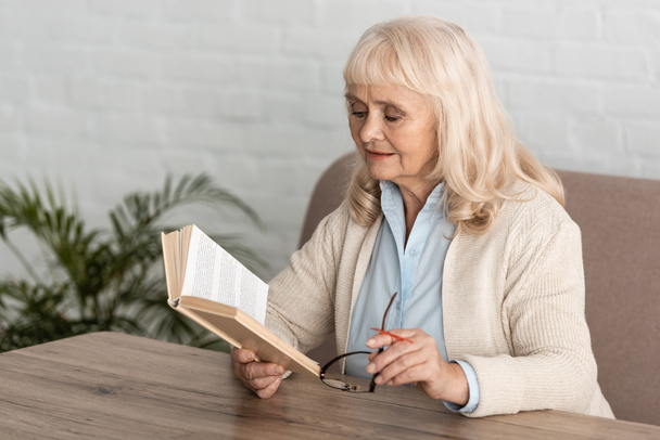 アルツハイマー病文字列人間の指のリマインダー読書本と保持眼鏡を持つシニア女性 - 写真・画像