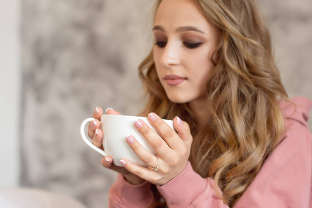 Teen girl sits on a bed in a winter warm sweater enjoying delicious homemade fruit tea. - Photo, Image