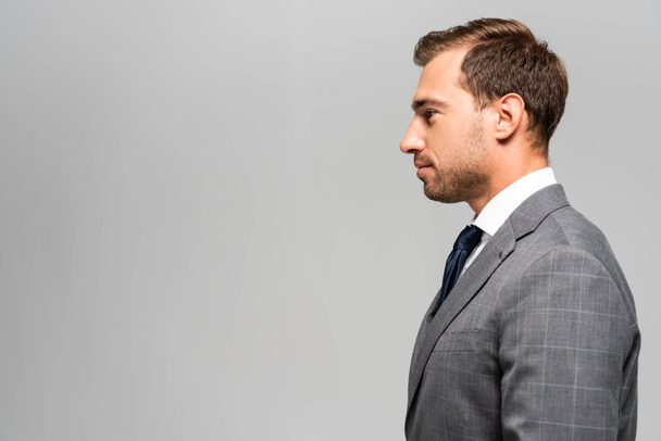 side view of handsome businessman in suit isolated on grey  - Foto, imagen