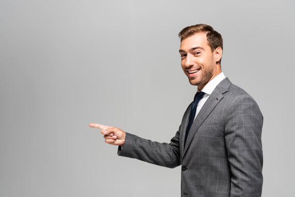 smiling and handsome businessman in suit pointing with finger isolated on grey  - Photo, image