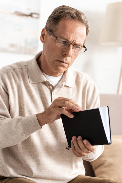senior man with alzheimer disease holding notebook at home  - Photo, Image