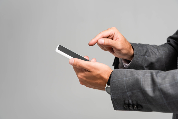 cropped view of businessman in suit pointing with finger at smartphone isolated on grey  - Фото, зображення