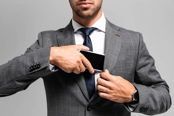 cropped view of businessman in suit hiding smartphone isolated on grey  - Foto, afbeelding