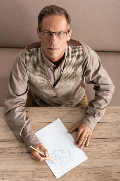 top view of senior man in glasses holding pencil while drawing picture  - Foto, imagen