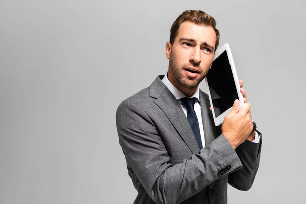 handsome businessman in suit using digital tablet isolated on grey  - Fotó, kép