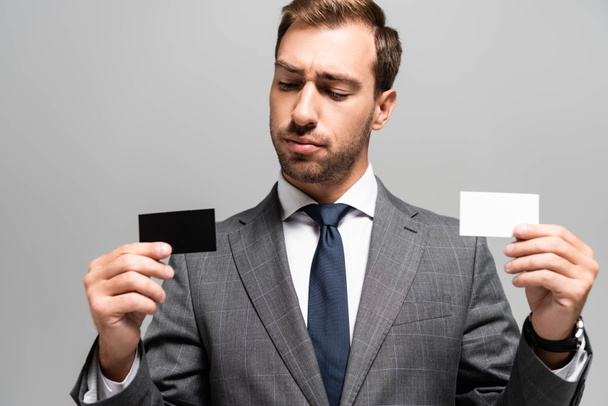 schöner Geschäftsmann im Anzug mit Visitenkarten isoliert auf grau  - Foto, Bild