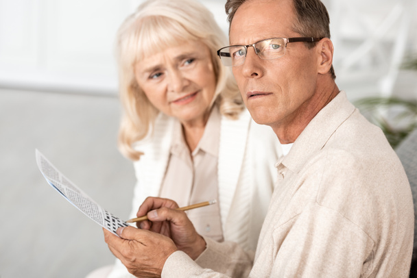 szelektív fókusz beteg idős férfi Alzheimer gazdaság ceruza közelében keresztrejtvény és feleség  - Fotó, kép