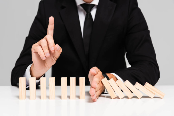 cropped view of businessman in suit preventing wooden blocks from falling and showing idea sign isolated on grey  - Photo, image