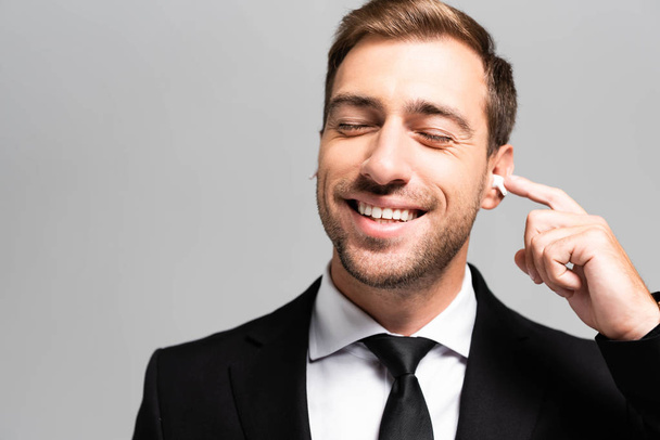 handsome and smiling businessman in suit listening music isolated on grey  - Foto, imagen