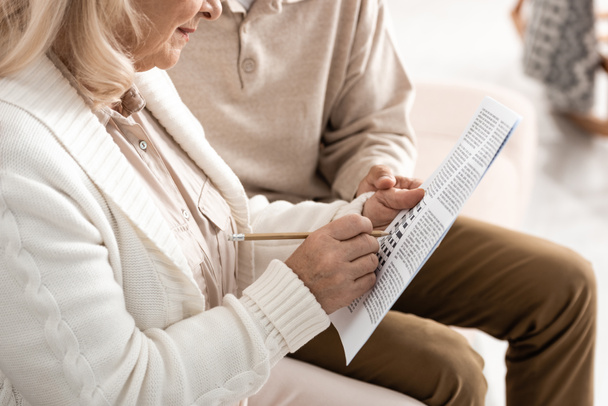 обрезанный вид пожилого человека, сидящего с женой, решающего кроссворд
  - Фото, изображение