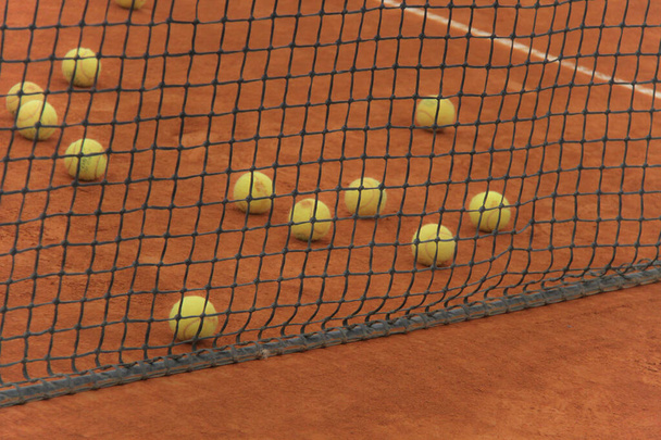 Pelotas de tenis en pista roja con red gris
 - Foto, Imagen