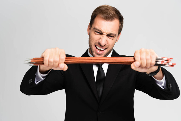 angry and handsome businessman in suit breaking arrows isolated on grey - 写真・画像