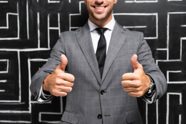 cropped view of smiling businessman in suit showing thumbs up near labyrinth - Фото, зображення