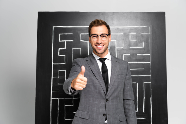 knap en lachend zakenman in pak tonen als en staan in de buurt van labyrint - Foto, afbeelding
