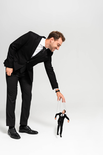 sonriente hombre de negocios en traje jugando con marioneta sobre fondo gris
  - Foto, Imagen