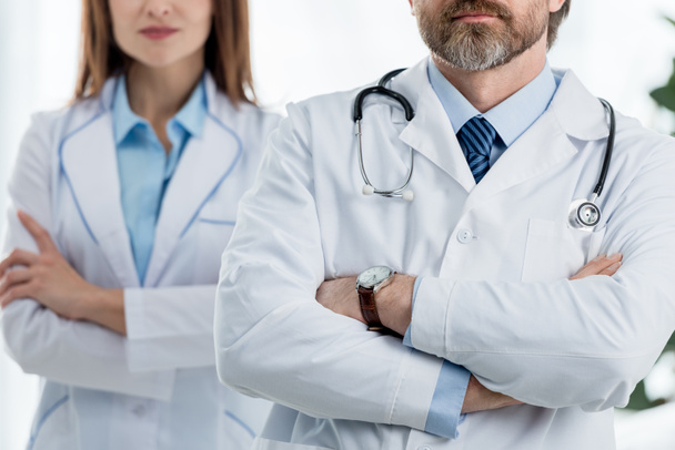 Ausgeschnittene Ansicht von Ärzten in weißen Mänteln mit verschränkten Armen im Krankenhaus  - Foto, Bild