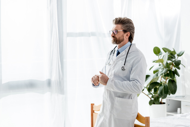 白衣を着たハンサムな医者が病院でスマホで話すポケットに手を入れて ロイヤリティフリー写真 画像素材