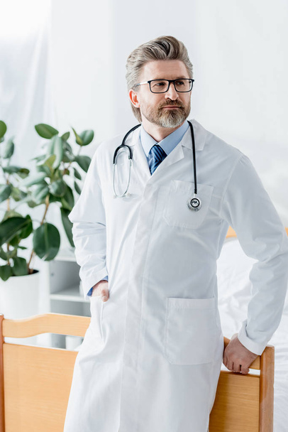 handsome doctor in white coat looking away in hospital  - Фото, зображення