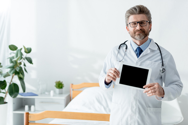 病院にコピースペースのあるデジタルタブレットを持っている白いコートの笑顔の医者  - 写真・画像