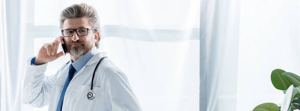 Beyaz önlüklü doktorun hastanede akıllı telefondan konuşmasının panoramik görüntüsü.  - Fotoğraf, Görsel
