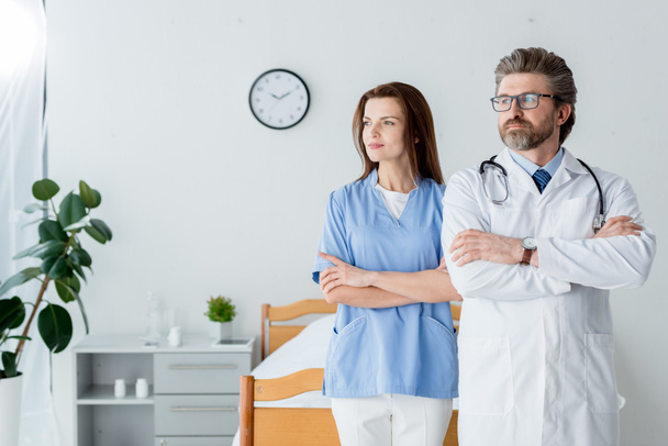 lékař v bílém plášti a atraktivní zdravotní sestra se zkříženýma rukama odvrací pohled v nemocnici  - Fotografie, Obrázek