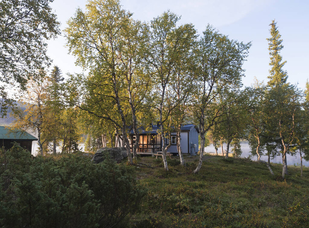 パルテFjallstugaでの朝の日の出湖Sjabatjakjaure 、緑の丘や白樺の木とStfマウンテンキャビン小屋。クングスレーデン・トレイルのスウェーデン・ラップランド - 写真・画像