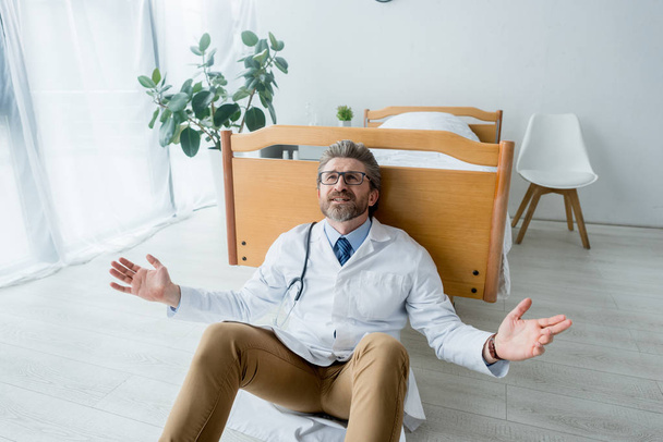 triste médico de bata blanca sentado en el suelo con las manos extendidas en el hospital
  - Foto, Imagen