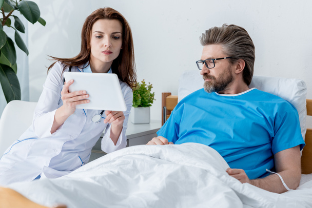 lääkäri valkoisessa takissa ja potilas katselee digitaalista tablettia sairaalassa
  - Valokuva, kuva