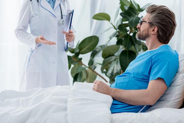 καλλιεργημένη άποψη του γιατρού με λευκό παλτό μιλώντας με ασθενή στο νοσοκομείο  - Φωτογραφία, εικόνα