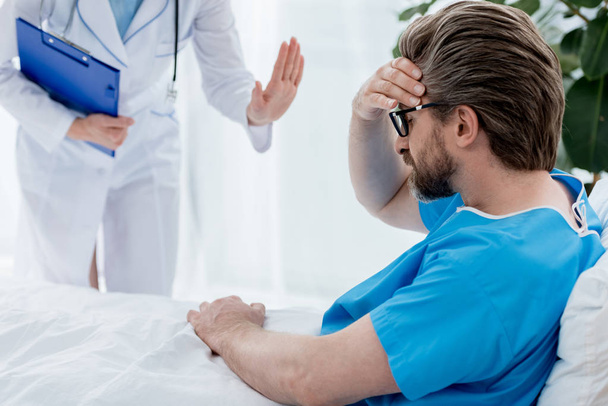 bijgesneden zicht van arts in witte jas kalmerende trieste patiënt in het ziekenhuis  - Foto, afbeelding