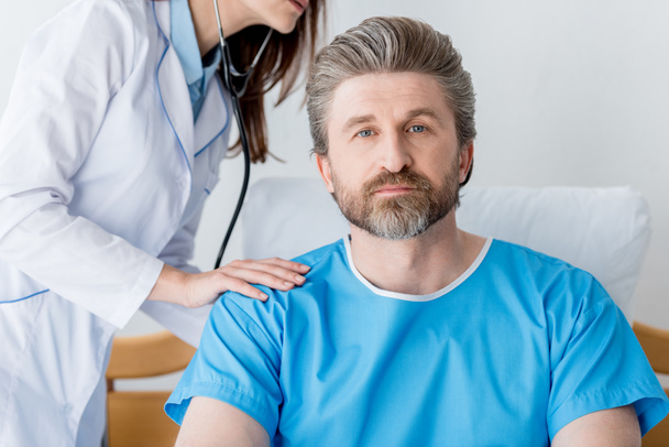 przycięty widok lekarza w białym płaszczu badającego pacjenta stetoskopem w szpitalu  - Zdjęcie, obraz