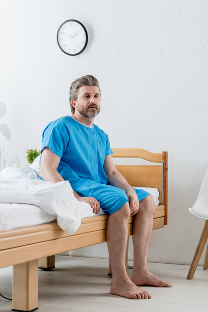 beteg orvosi köntösben ül az ágyon és félrenéz a kórházban  - Fotó, kép