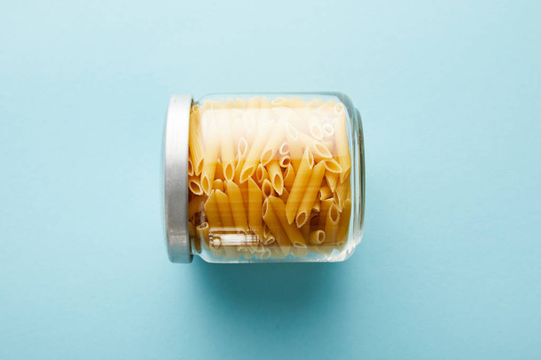 top view of raw penne in jar on blue background with copy space - Fotoğraf, Görsel