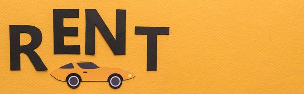 top view of paper cut car and black rent lettering on orange background with copy space, panoramic shot - Photo, Image