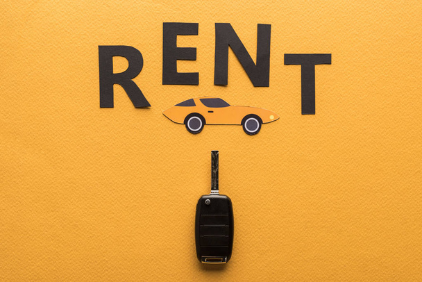 top view of car key, paper cut auto and black rent lettering on orange background - Photo, Image