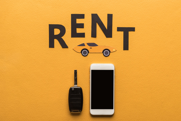 top view of smartphone with blank screen, car key, paper cut auto and black rent lettering on orange background - Photo, Image
