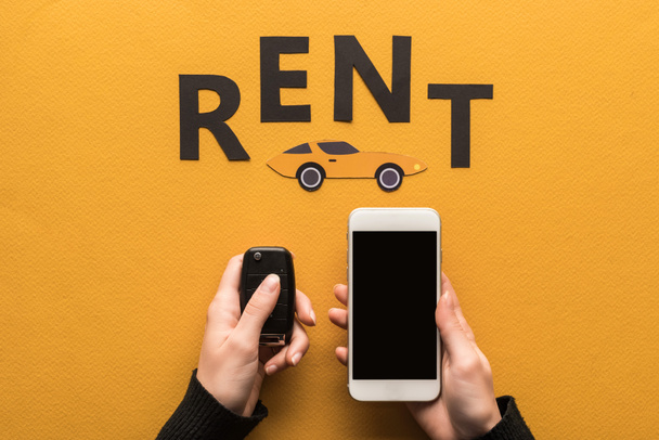 車のキーを持っている女性と紙の近くのスマートフォンのクロップドビューオレンジの背景に自動車と黒の賃貸料のレタリング - 写真・画像