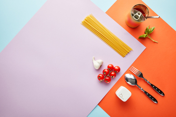 flache Lage mit leckeren Spaghetti mit Zutaten für Tomatensauce auf rotem, blauem und violettem Hintergrund - Foto, Bild