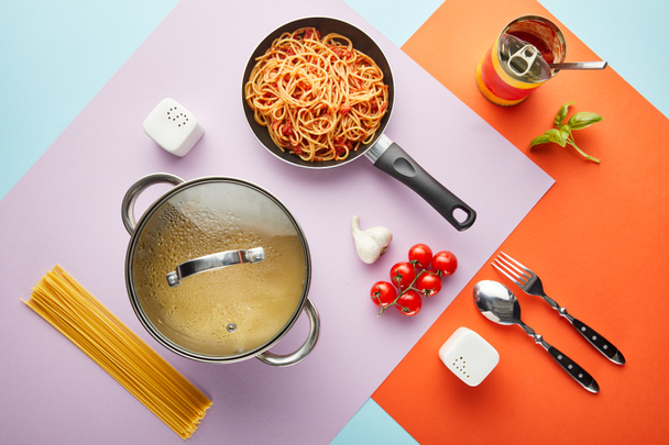 flat lay with delicious spaghetti with tomato sauce ingredients and cooking utensils on red, blue and violet background - Photo, Image