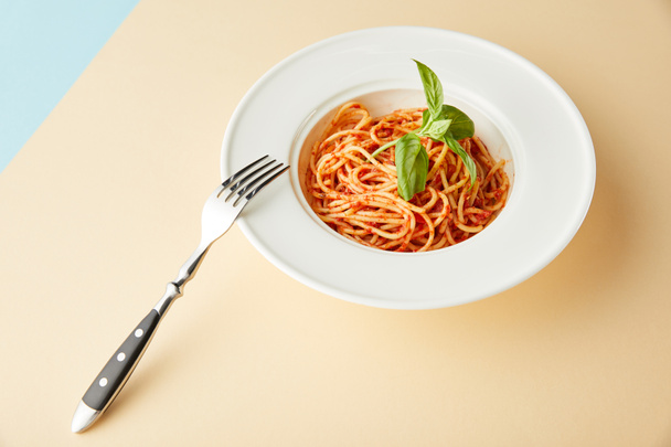 spaghetti met tomatensaus in bord bij vork op blauwe en gele achtergrond - Foto, afbeelding