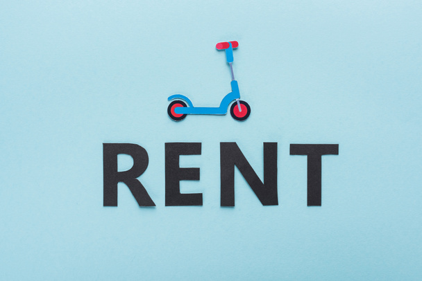 top view of paper cut kick scooter and black rent lettering on blue background - 写真・画像