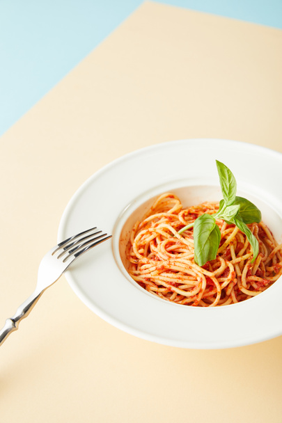 leckere Spaghetti mit Tomatensauce in Teller in der Nähe Gabel auf blauem und gelbem Hintergrund - Foto, Bild