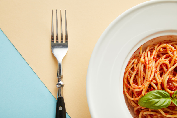 top view of delicious spaghetti with tomato sauce in plate near fork on blue and yellow background - Fotó, kép