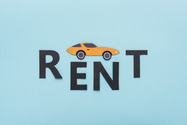 top view of paper cut sports car and black rent lettering on blue background - Foto, imagen